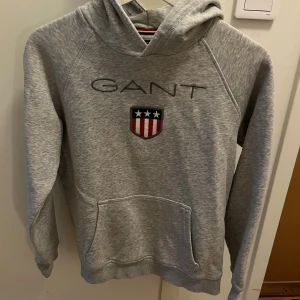 Grå Gant hoodie 158/164 - Grå Gant Hoodie med huva och magficka fram. Storlek 158/164, 13-14 år. 