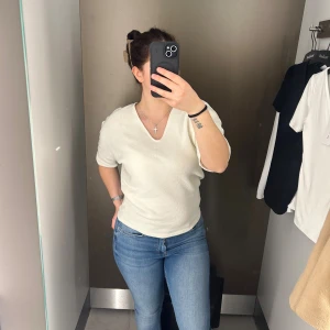 Vit ribbad topp med v-ringning - Säljer en stilren crèmefärgad topp med v-ringning och korta ärmar. Toppen är ribbad och har en avslappnad passform som gör den enkel att styla. Perfekt för dig som gillar en clean och enkel look. Materialet känns mjukt och bekvämt mot huden. Den är köpt på second hand och har inga lappar på sig, så vet inte vilket märke det är. Det står inte heller någon storlek men skulle tippa på S/M 