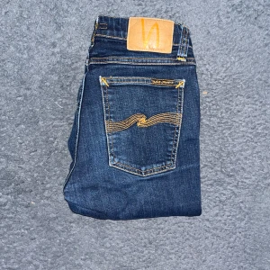 Nudie Jeans  - Mörkblå skinny jeans från Nudie Jeans, modell Skinny Lin. Snygga kontrastsömmar i orange och klassisk femficksdesign. Tillverkade i 99% ekologisk bomull och 1% elastan för en tight passform. OBS GYLFEN FUNKAR EJ dragkedjan har lossnat med kan skicka med den om det önskas  Ifall det inte finns någon bild i annonsen där jag bär plaggen jag säljer så är det för att jag ej kan ha storleken heller passformen, så kolla måtten för storlek och googla på modellnamnet för passform 😉
