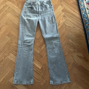 Grå bootcut jeans, stl 158 - Snygga grå jeans med bootcut passform. Jeansen har medel midja och är tillverkade i stretchigt denimtyg för extra komfort. Dessa jeans har dock ett hål i högra bakfickan. De går att sy igen om man vill. 