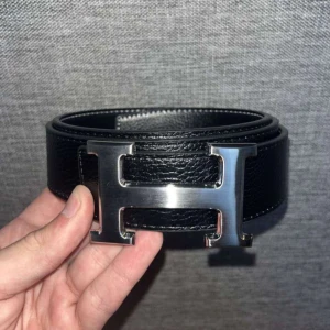 Svart Herm skärp med H-spänne - Herm bälte – svart med silverspänne, 110 cm  Snyggt och klassiskt Herm-bälte i svart med silverspänne. Längd 110 cm med 5 hål för justering.  Färg: Svart Spänne: Silver Längd: 110 cm Skick: Oanvänt Snabb leverans. 