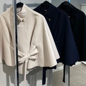 PONCHO BLAIR JACKA - Säljer en beige kappa med högt krage, vida ärmar och snyggt bälte i midjan. Jackan har en guldfärgad knapp upptill och ett stilrent, minimalistiskt uttryck. Perfekt för dig som gillar clean och elegant stil.