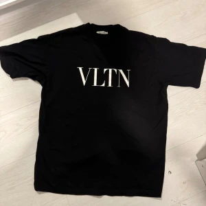 Svart VLTN t-shirt från Valentino - Svart t-shirt från Valentino med VLTN-tryck i vitt på bröstet. Klassisk passform med korta ärmar och rund halsringning. Tillverkad i 100% bomull för en skön och mjuk känsla. Perfekt för dig som gillar stilrena designer och exklusiva märken. Storlek S sitter som M