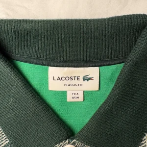 Grön mönstrad piké från Lacoste.  - Snygg grön pikétröja från Lacoste med klassisk krage och vit knappslå. Använd ungefär 5 gånger, detta är en limited edition version så det tillkommer även med en liten kartong och fin paketering. Priset kan diskuteras då jag försöker bli av med så mycket som möjligt.