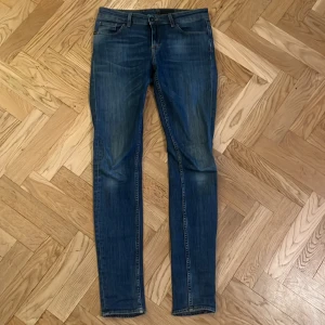 Tiger of Sweden blå jeans Slight 29/34 - Snygga blå jeans från Tiger of Sweden i modellen Slight. De har en klassisk femficksdesign, smal passform och är tillverkade i mjukt jeanstyg. Perfekta för dig som gillar stilrena och moderna jeans med lite slitningar för en cool look.