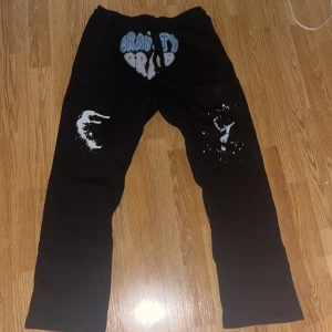 Svarta Gravity Grub mjukisbyxor - Svarta mjukisbyxor från Gravity Grub med broderad logga i blått och vitt framtill. Byxorna har snörning i midjan och coola vita tryck på benen. Mjukt material och en bakficka. Perfekta för chill eller streetwear. Kom med bud