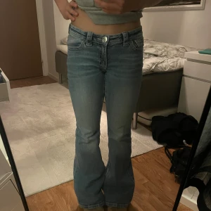 Ljusblå bootcut jeans  - Säljer ett par ljusblå bootcut jeans med låg midja och snygga strassdetaljer på bakfickorna. Jeansen har klassisk femficksdesign och är tillverkade i mjukt denimtyg. Perfekta för dig som gillar en retro vibe och vill sticka ut lite extra. Jag är 168 cm och passar ganska perfekt! Storlek: 164
