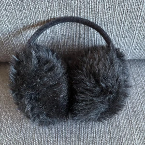 Svarta fluffiga öronmuffar - Mysiga svarta öronmuffar med superfluffig pälsimitation. Bågen är klädd i mjukt tyg och sitter bekvämt på huvudet. Dom är för små för mig, så en bit av mina öron täcks inte. Använda nån gång!