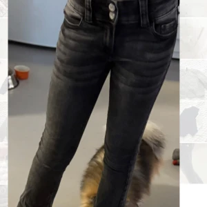 Svarta  jeans med dubbla knappar - Snygga svarta skinny jeans med cool tvättad look och dubbla knappar i midjan. Fickor med lock och silverfärgade knappar bak ger extra stil. Jeansen har smal passform och är perfekta för dig som gillar en modern och tajt siluett.