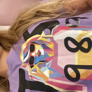 Lila Taylor Swift t-shirt med 1989-tryck och popart ✨💖✨ - Lila t-shirt med coolt popart-tryck av Taylor Swift med solglasögon och texten 'TS 1989' på bröstet. Färgglad design i rosa, blått, gult och svart. Klassisk passform och rund hals. Perfekt för dig som gillar Taylor, färg och statement-plagg! 💞💞💞