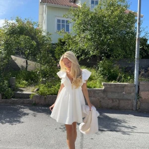 Vit klänning från Showpo - Supersöt vit kortklänning med djup v-ringning, volangärmar och öppen rygg med rosett. Klänningen har en flowy passform och är tillverkad i mjukt bomullstyg. Perfekt för studenten! Köpt här på plick men säljer pågrund av att den ej passade mig. Ej använd bara testad, prislapp finns kvar! Storlek xs, justerbar i ryggen. Från Showpo, slutsåld på hemsidan! Pris kan diskuteras.