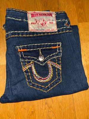 True Religion Billy Super T Row Seat – W31 – Nyskick – Made in USA - .Äkta True Religion Billy Super T Row Seat jeans i mycket bra skick (nyskick). Klassisk Super T-modell med kraftiga sömmar och broderade bakfickor. Tillverkade i USA i denim av hög kvalitet med lätt stretch.  Detaljer: 	•	Storlek: W31 (herr) 	•	Material: 99 % bomull, 1 % elastan 	•	Färg: Mörkblå 	•	Made in USA  Mått (platt mätt): 	•	Midja: 41 cm 	•	Innerben: 80 cm 	•	Ytterlängd fram/bak: 100 / 106 cm
