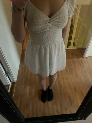 Vit jumpsuit med puffärm och knyt - Supersöt vit jumpsuit med puffärmar och strukturmönster. Har en öppen rygg med en rosett. Lite vit gulfärgad men inte så mycket. 