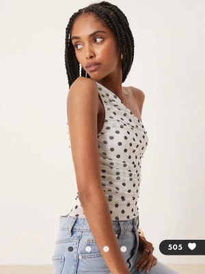 Vit prickig oneshoulder body - Säljer en vit oneshoulder topp med svarta prickar. Toppens material är lätt och stretchigt, och den har en tight passform som framhäver siluetten. Perfekt till jeans eller kjol för en trendig look. Obs en body💗att xs❤️helt ny