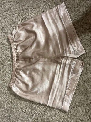 Ljusbeige sovshorts i satin - Säljer ett par ljusbeige sovshorts i satinliknande material. De har elastisk midja och en liten slitsdetalj på sidan av benen.