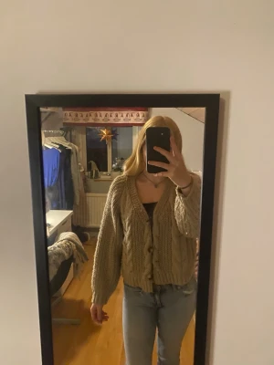 Beige stickad kofta med knappar - Säljer en mysig beige stickad kofta med grova flätstickade detaljer och stora knappar framtill. Koftan har långärmade, lite puffiga ärmar och en v-ringad hals. Perfekt att slänga på sig när det är kyligt ute. Nypris 699