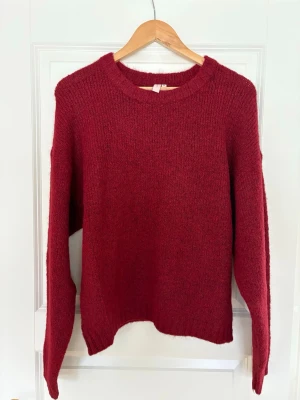 Mysig vinröd stickad tröja M oanvänd  - Enkel och snygg vinröd stickad tröja med rund hals och långa ärmar. Perfekt för kyliga dagar och lätt att matcha med jeans eller kjol. Tröjan har en mjuk och fluffig känsla som gör den superbekväm att bära.