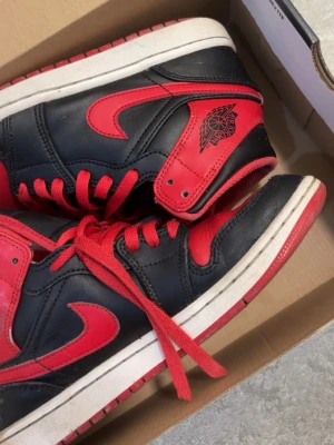 Nike Air Jordan 1 High svart/röd - Örebro. . Säljer ett par Nike Air Jordan 1 High i klassisk svart och röd färg. Skorna har röd swoosh, röda snören och detaljer samt svart läder på ovandelen. Ikonisk Air Jordan-logga på sidan och perforerad tå för extra stil. Perfekta för dig som gillar streetwear och sneakerskultur. Pris kan diskuteras 
