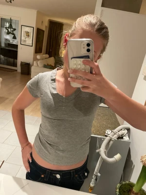 Grå v-ringad t-shirt 🩶 - Säljer en enkel och stilren grå t-shirt med v-ringning. T-shirten är kortärmad och har en tight passform som sitter snyggt. Perfekt basplagg i mjuk bomull som funkar till allt. Snygg att matcha med jeans eller shorts 🤎🤎