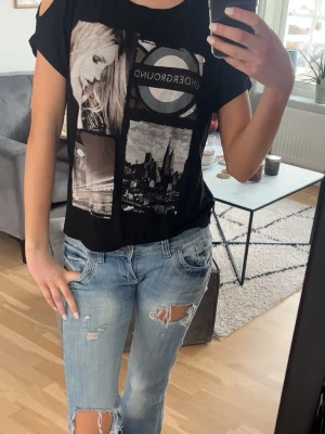 Skit cool underground T-shirt - Svart t-shirt med coola citymotiv och Underground-tryck framtill. Modellen har korta ärmar med trendiga cut out-detaljer på axlarna. Skön passform och mjukt material, perfekt till jeans för en avslappnad look.