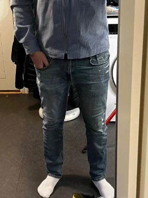 Replay blå slitna jeans - Säljer ett par blå jeans från Replay med slitningar och snygga detaljer.W32/L32Materialet är jeans och färgen är en tvättad blå ton med ljusare partier och slitna effekter på framsidan.