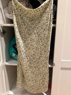 Ljus långklänning med prickigt mönster - Säljer en ljus långklänning med tunna axelband och ett prickigt mönster i svart och lila. Klänningen har en mjuk, glansig yta som ger ett lyxigt intryck och faller snyggt längs kroppen. Perfekt för dig som gillar en stilren men ändå lekfull look.