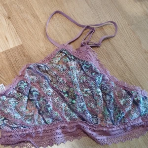 Paisleymönstrad spets croptop Victoria's Secret - Superfin croptop från Victoria's Secret i paisleymönster med lila och gröna toner. Topp med tunna axelband, spetsdetaljer och mjuk, stretchig känsla. Perfekt för sommarvärmen eller som statement piece under en öppen skjorta.