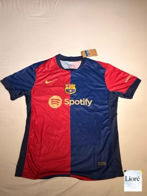 Barcelona Fotbollströja Halv Blå / Halv Röd Spotify Herr S/M - Säljer en FC Barcelona-tröja med unik design: halva tröjan blå och halva röd. Tröjan har sponsortrycket "Spotify" på framsidan. Perfekt för fotbollsfans, samlare eller vardagsbruk.    - Märke: FC Barcelona   - Typ: Fotbollströja   - Storlek: S/M  - Skick: Ny   - Material: Polyester / Bomull (om du vet)    Snabb och trygg frakt. Passa på innan den är borta!
