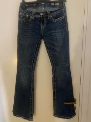 Miss Me blå bootcut jeans strl 28 - Säljer ett par blå jeans från Miss Me i bootcut-modell med kontrastsömmar och detaljerade bakfickor med knappar och broderi. Lite slitna ner till men annars ingen skada💓