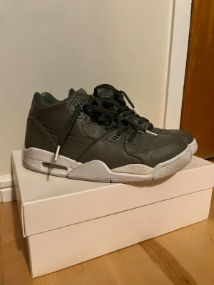 NikeLab Air Flight 89 sneakers grön - NikeLab Air Flight 89 sneakers i mörkgrönt skinn med vita sulor. Klassisk retrobasketstil med rund tå, snörning och vadderad plös. Swoosh-logga på sidan och Nike-broderi bak. Snygg chunky siluett som passar till streetwear.