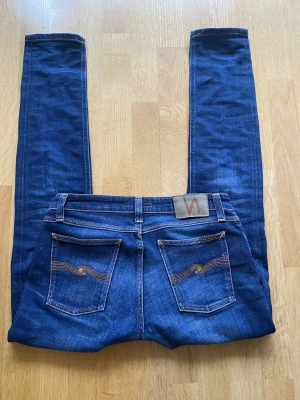 Nudie Jeans W30 L32 - Mörkblå jeans från Nudie. Klassisk femficksdesign med orangea sömmar och Nudie-logga på bakfickan.  De är proffsigt lagade i skrevet men det syns inte alls när de är på. Pris går att diskutera och skriv vid frågor:)