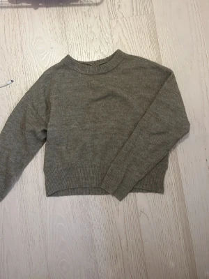 Beige stickad tröja från Vero Moda - Mysig beige stickad tröja från Vero Moda i croppad modell. Tröjan har rund hals, ribbade muddar vid ärmslut och nederkant samt lång ärm. Perfekt till höst och vinter för en enkel men snygg look.