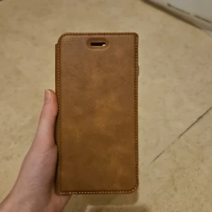 Mobilskal för iphone 7 plus och 8 plus - Säljer ett helt oanvänt plånboksfodral i brunt konstskinn som passar till iPhone 7 Plus och iPhone 8 Plus. ​Skick: Aldrig använt, helt nyskick. ​Passar: iPhone 7 Plus och iPhone 8 Plus. ​Funktion: Plånboksmodell med plats för kort och skyddande skal.