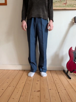 Blå kostymbyxor med rak passform - Säljer ett par stilrena blå kostymbyxor med rak passform. Byxorna har pressveck framtill och klassisk midja. Perfekta för dig som vill ha en clean och enkel look. Materialet känns lätt och smidigt.