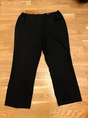 Svarta raka byxor från Facit - Säljer ett par svarta byxor från Facit med rak passform och enkel design. Byxorna är tillverkade i 100% polyester och har en knapp framtill. Perfekta för dig som gillar stilrena och klassiska plagg. XL-L