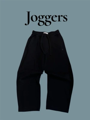 Svarta mjukisbyxor Pull&Bear XS - Svarta mjukisbyxor från Pull&Bear i storlek XS. Byxorna har dragsko i midjan, fickor fram och en bakficka. Tillverkade i mjukt bomullsmaterial och har en relaxed, loose passform. Diskret Pull&Bear-logga på ena benet.