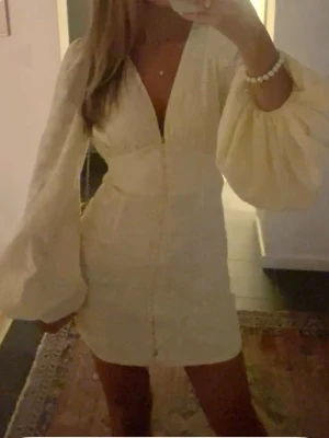 Vit kort klänning med puffärmar - Superfin vit kort klänning med broderade blommor, djup v-ringning och stora puffärmar. Klänningen har knappar framtill och markerad midja som ger en snygg siluett. Perfekt för sommarens alla tillfällen!