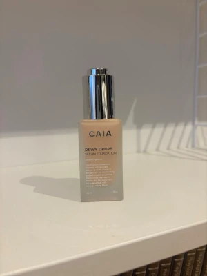 CAIA Dewy Drops Serum Foundation 10C - Foundation från CAIA i nyansen 10C. Aldrig använd. Kommer i en frostad glasflaska med silvrig pump. Ger en naturlig, daggig finish och innehåller vitamin E och glycerin för återfuktning. Perfekt för dig som vill ha en lätt och fräsch bas.