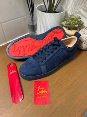 Marinblå mockasneakers Christian Louboutin - FINNS I STORLEK 41 & 43 ‼️Snygga marinblå sneakers från Christian Louboutin i mjuk mocka med klassisk röd sula och rund tå. Skorna har snörning och diskret broderad logga på hälen. Insidan är fodrad i ljust skinn för extra komfort. Perfekta för dig som vill ha något exklusivt och stilrent. 