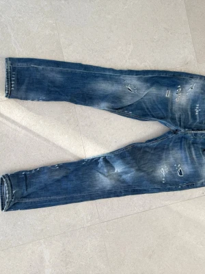 Blå slitna jeans med raka ben - Säljer ett par blå jeans från Dondup. Jeansen har ett reparerat hål mellan benen men annars i fint skick.