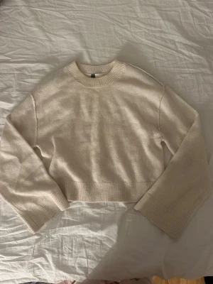 Beige croppad stickad tröja H&M - Säljer en beige croppad stickad tröja från H&M Divided. Tröjan har breda ribbade muddar vid ärmslut och nederkant, rund halsringning och lång ärm. Perfekt till lager på lager och enkel att styla till olika outfits.
