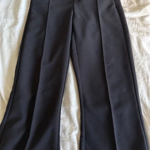 Svarta kostymbyxor från Gina Tricot XS - Svarta kostymbyxor från Gina Tricot i storlek XS. Byxorna har raka ben, pressveck framtill och klassisk knäppning med både hake och knapp. Snygg passform och stilren look, perfekta till en trendig outfit.