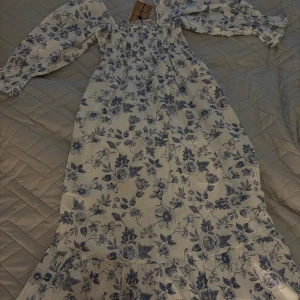 Klänning  - Pris går att diskutera! Helt ny och oanvänd klänning! Klänningen sitter löst och skönt men tajtare över bysten, den är vit med blåa blommor. Den var jätte populär och svar snabbt slutsåld på hemsidan samt i butik när den var aktuell. Kostar egentligen 699kr