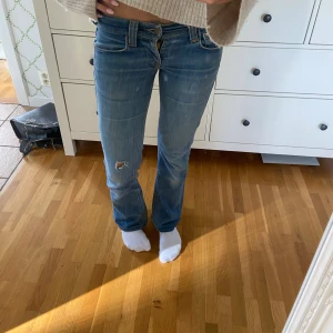Blå bootcut low waist jeans  - Snygga blå jeans från 2000s med bootcut-modell och låg midja. Jeansen har slitning och ett hål på ena benet. De har blivit för korta därför säljer jag de. Längst ner har jag fått sprätta de. Storlek vet jag inte exakt men skulle säga xs/s 32/34