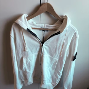 Vit hoodie från Stone Island - Vit hoodie från Stone Island, tröjan är i storlek . Tillverkad i mjuk bomull Perfekt för dig som vill bära kläder med stil. Väldigt bra skick, lite skrynklig då den har legat i min garderob ett tag👍