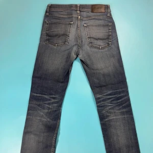 Blå jeans från Jack & Jones - Snygga blå jeans från Jack & Jones med klassisk femficksdesign och slitna detaljer framtill. Jeansen har normal passform och raka ben, tillverkade i mjukt denimtyg. Perfekta för en avslappnad stil och funkar året runt.