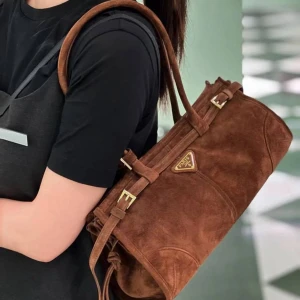 Brun mocka axelväska Paris - Snygg brun axelväska i mocka med guldiga spännen och detaljer. Väskan har en avlång form, dubbla handtag och en klassisk Paris-logga framtill. Perfekt för dig som vill ha en trendig och stilren accessoar med vintagekänsla.