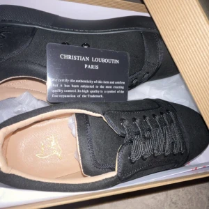 Svarta sneakers från Christian Louboutin - Snygga svarta sneakers från Christian Louboutin med klassisk design och diskret logga på innersulan. Skorna har svart snörning, rund tå och är tillverkade i mocka med detaljer i skinn. Perfekta för dig som vill ha en stilren och exklusiv look.