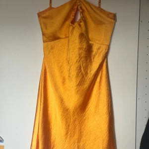 Gul långklänning från Gina Tricot - Superfin gul långklänning från Gina tricot med snygg cut-out och knytning i ryggen. Klänningen har en glansig satinliknande yta. Perfekt för dig som vill sticka ut med färg och coola detaljer.