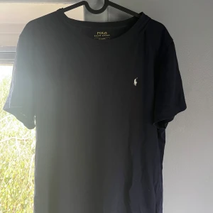 Mörkblå t-shirt från Polo Ralph Lauren - Klassisk mörkblå t-shirt från Polo Ralph Lauren i bomull med broderad logga på bröstet. Enkel och stilren design med rund hals och korta ärmar. Perfekt för en clean och tidlös look.